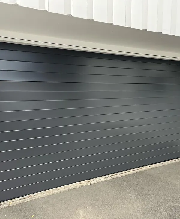 Dark gray modern flush-panel garage door on a white building