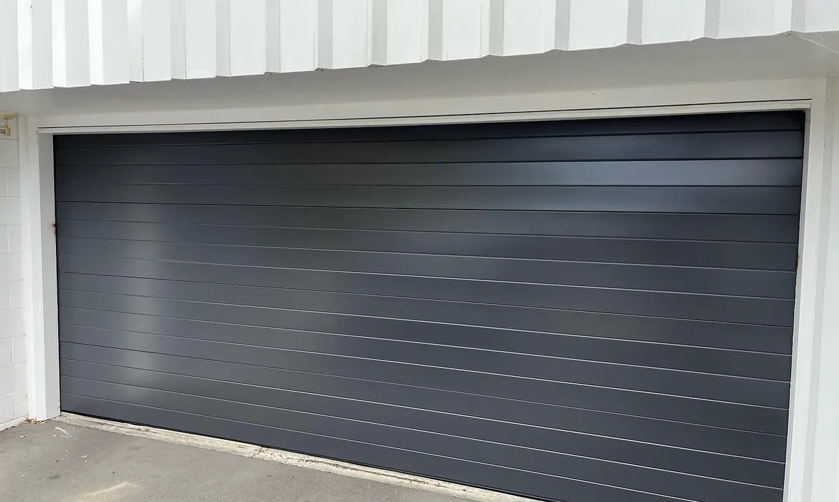 Dark gray modern flush-panel garage door on a white building