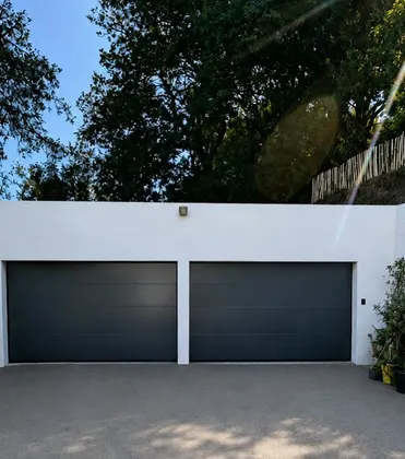 Two dark garage doors in a white courtyard